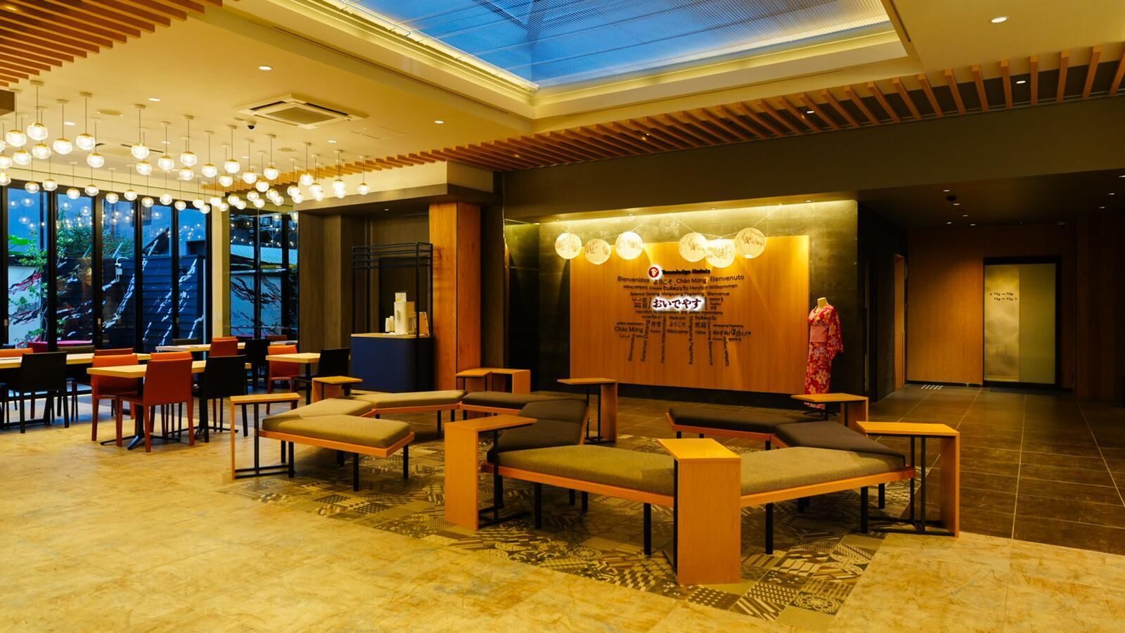 A modern hotel lobby with a reception desk, seating area, and a large screen displaying welcome messages.
