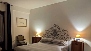 Une chambre avec un grand lit, deux tables de chevet avec des lampes, une chaise, un tableau encadré au mur et un plancher foncé.