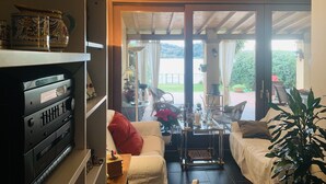 Un salon comprenant un canapé, une table basse et un meuble pour la télévision. Une porte-fenêtre coulissante donne accès à un patio extérieur aménagé avec une table et des chaises.