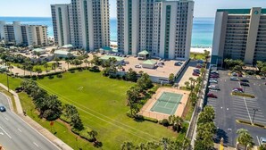 A high-rise hotel with multiple floors, a central courtyard with a tennis court, and a parking lot. - 🦩Book Me Baby! Amazing Views ~ Two King Suites ~ Chasin' The Blues Away 🦩 (Destin)