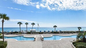 A resort pool area with a view of the ocean, palm trees, and a clear sky. - 🦩Book Me Baby! Amazing Views ~ Two King Suites ~ Chasin' The Blues Away 🦩 (Destin)