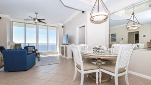 A spacious living area with a large dining table surrounded by white chairs, a blue sofa, and a ceiling fan. - 🦩Book Me Baby! Amazing Views ~ Two King Suites ~ Chasin' The Blues Away 🦩 (Destin)