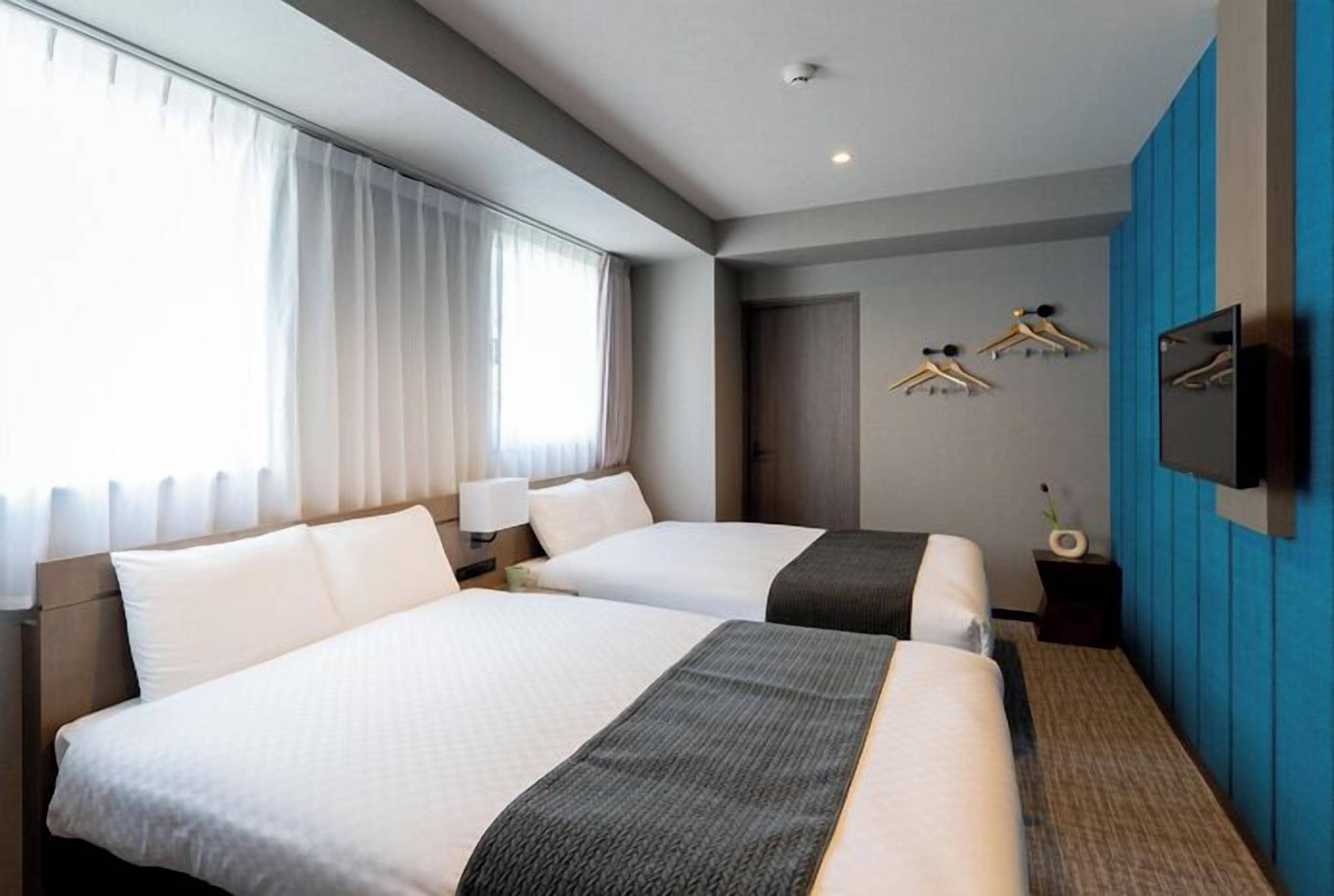 A hotel room with two beds, a television, a wardrobe, and a window with curtains.