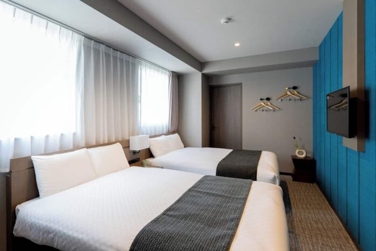 Habitación de hotel con dos camas, televisor, armario y ventana con cortinas.