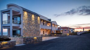 Un hotel moderno de varios pisos con fachada de piedra, balcones y una entrada con acceso por un camino.