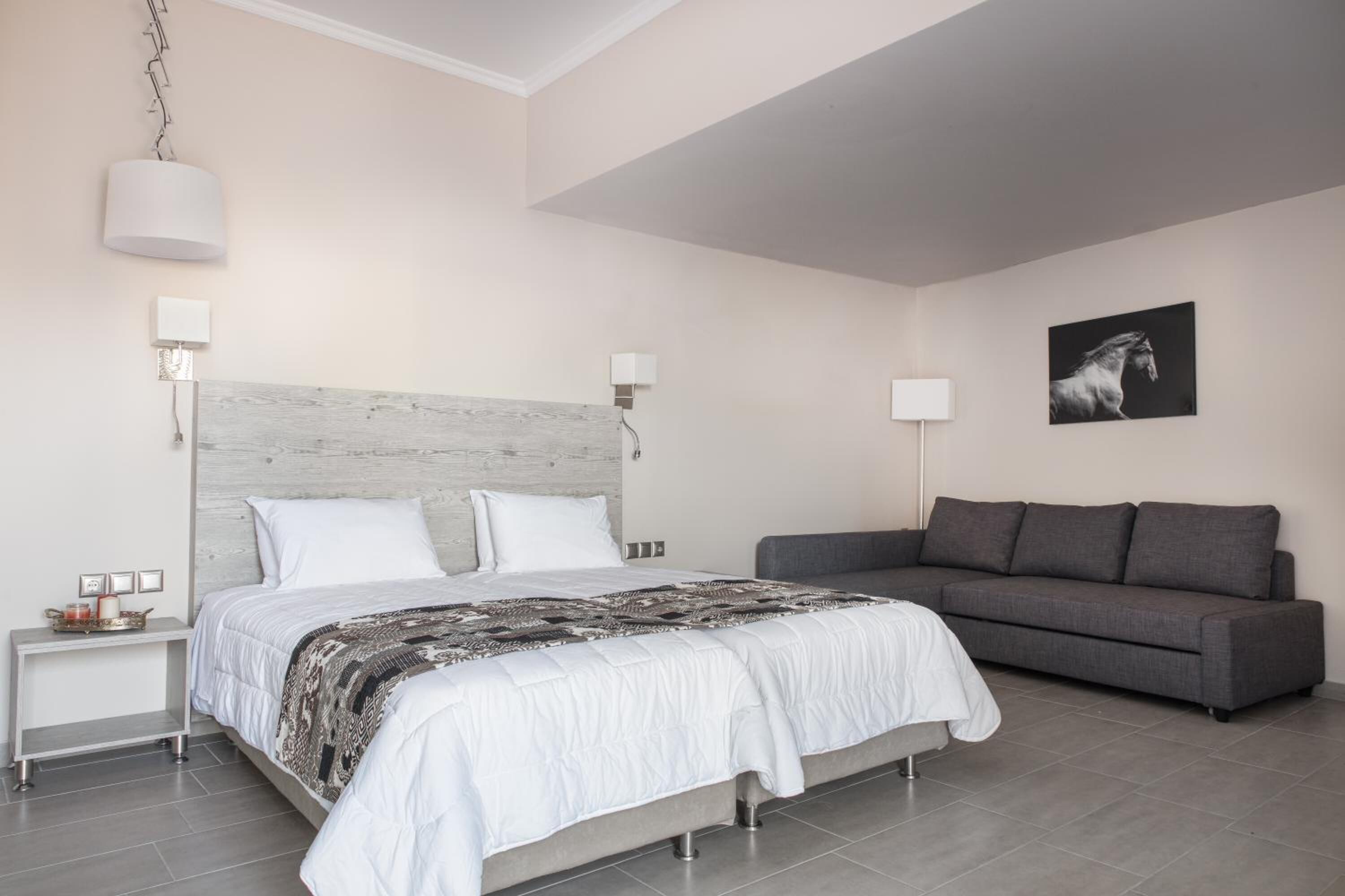 A modern bedroom with a large bed, a grey sofa, and a wall-mounted lamp.