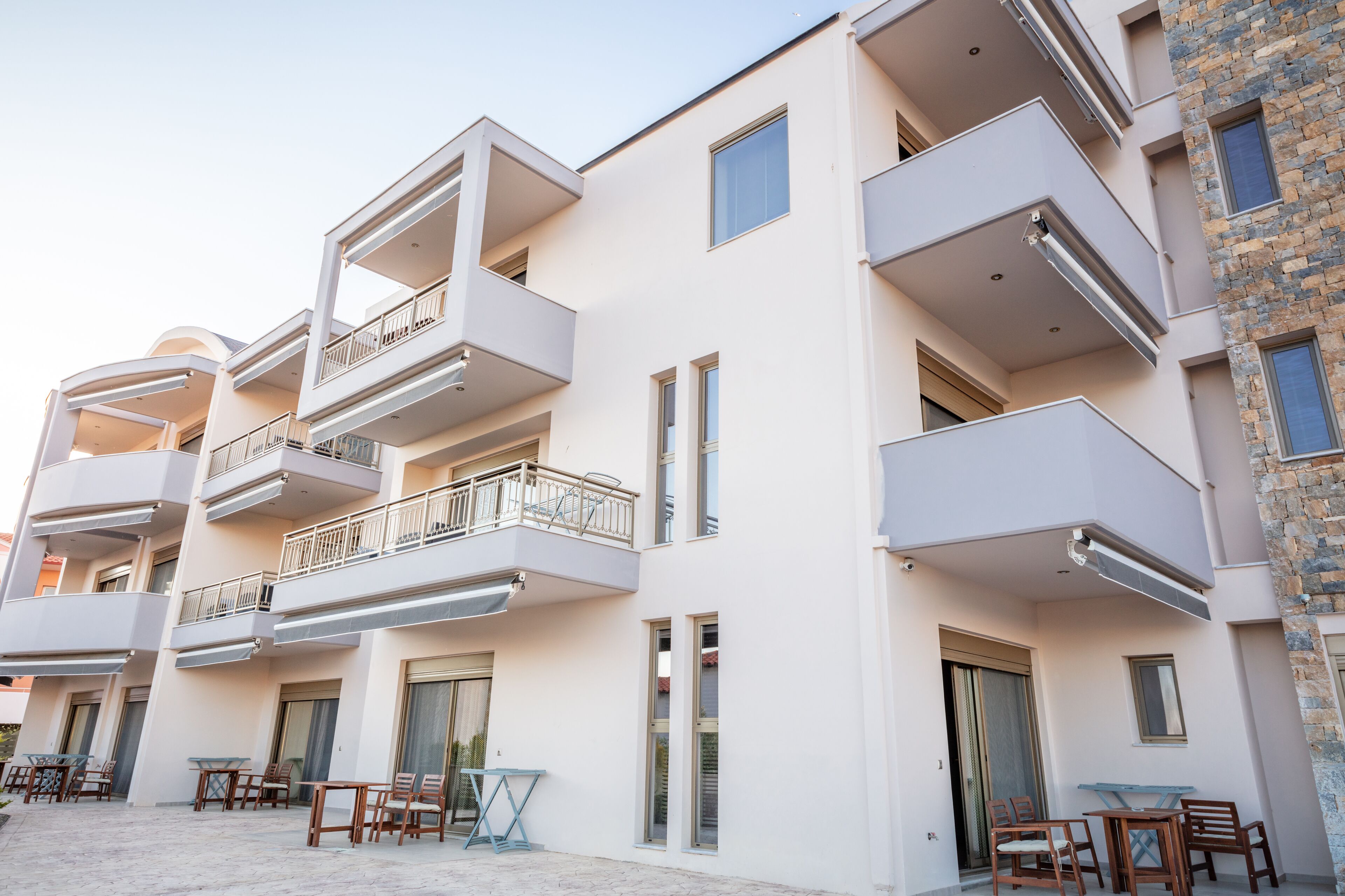 A multi-story building with balconies, outdoor seating, and a stone facade.