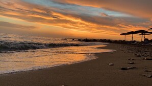 Una playa con sombrillas y sillas reclinables, una orilla arenosa y olas.