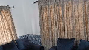 En stue med to mørkeblå sofaer og matchende puder, et flisegulv og gardiner med blomstermønster.