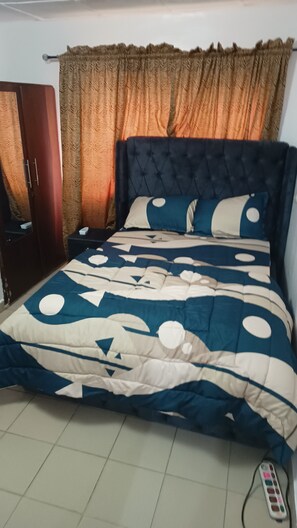 Une chambre à coucher avec un lit, des rideaux, une armoire et une télécommande posée sur le sol.