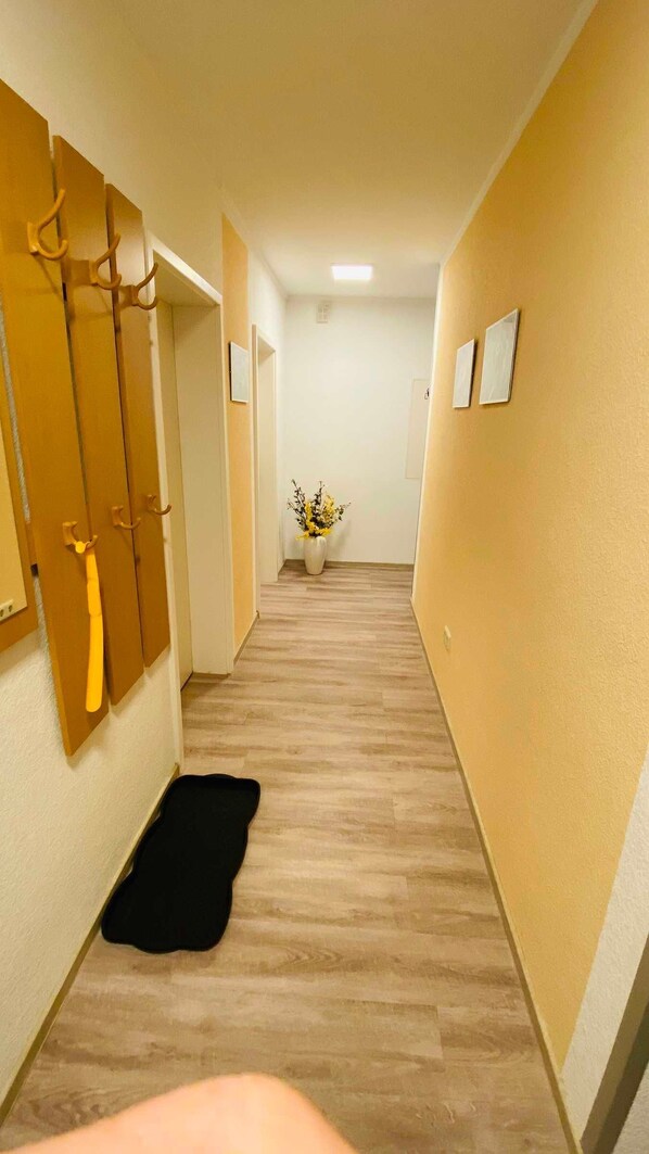 A hallway with wooden flooring, a black rug, a vase with flowers, and a coat rack.