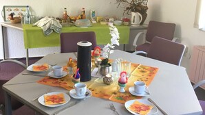 A dining area with a table set for four, chairs, a green tablecloth, and a painting of a bridge on the wall.