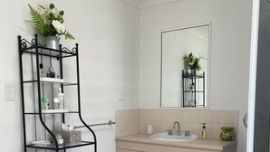 A bathroom with a beige vanity, a mirror, and a black metal shelf with towels. - BEACH, SHOPS & STRAND 5 min walk away (North Ward)