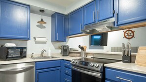 A kitchen with blue cabinets, a microwave, a stove, a sink, and a ship's wheel decoration.