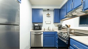 A compact kitchen with blue cabinets, a stainless steel refrigerator, a microwave, a sink, and a stove.