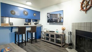A modern kitchen with blue cabinets, a bar area with stools, a mounted television, and a fireplace.