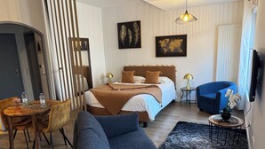 Una habitación de hotel moderna con cama, un sillón azul, una zona de comedor y televisión.
