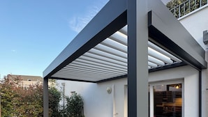 Un patio al aire libre con una terraza de madera, una mesa con sillas y una estructura de pérgola.