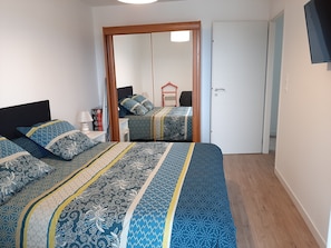 Un dormitorio con dos camas, un armario de madera, un espejo y un televisor en la pared.