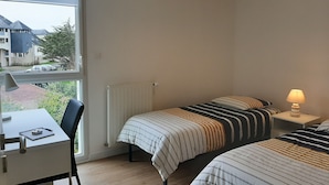A bedroom with two beds, a desk, and a window overlooking a street. - Superb T3 apartment in a quiet location overlooking the port of Crouesty (Arzon)
