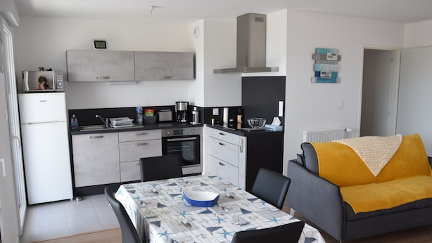 A compact kitchen with a microwave, toaster, and coffee maker. There is a dining table with chairs and a sofa with a yellow throw blanket. - Superb T3 apartment in a quiet location overlooking the port of Crouesty (Arzon)