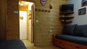Une pièce en bois avec un canapé, un téléviseur posé sur une étagère et une décoration en forme de cœur accrochée au mur.