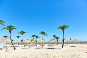 A beach with palm trees and thatched umbrellas. - Santorini Apartament (Navodari)