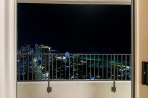 A night view from a balcony with a metal railing, overlooking a cityscape with illuminated buildings and a Ferris wheel.