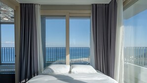 A hotel room with a large bed, two windows with curtains, and a view of the beach and ocean. - Hotel the Blue Terra (Sokcho)