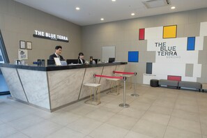 A reception area with a counter, two staff members, and a seating area with a red barrier.