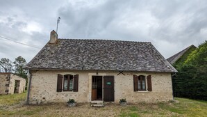 Une petite maison en pierre avec un toit en tuiles, une cheminée et une porte portant l’inscription « Site de… ».