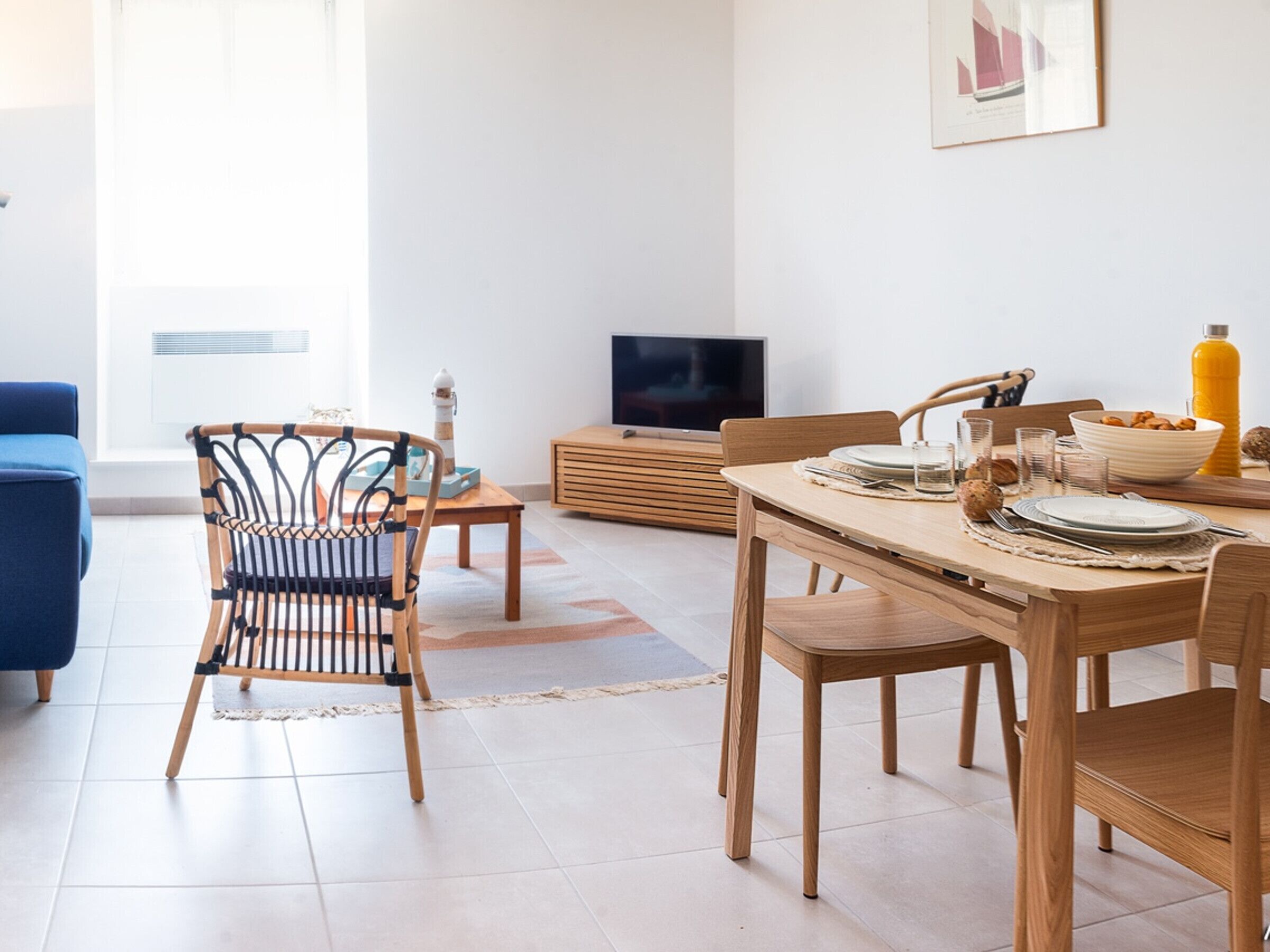 A modern living room with a dining area, featuring a TV, wooden furniture, and a large window.