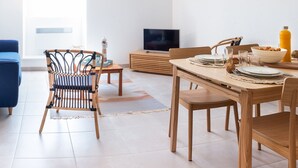 Una sala de estar moderna con comedor, que incluye un televisor, muebles de madera y un ventanal grande.