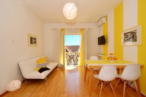 A bright living room with a white sofa, yellow cushions, a dining table with chairs, and a view of the outside. - Stunning Apartment in Bol (Bol)