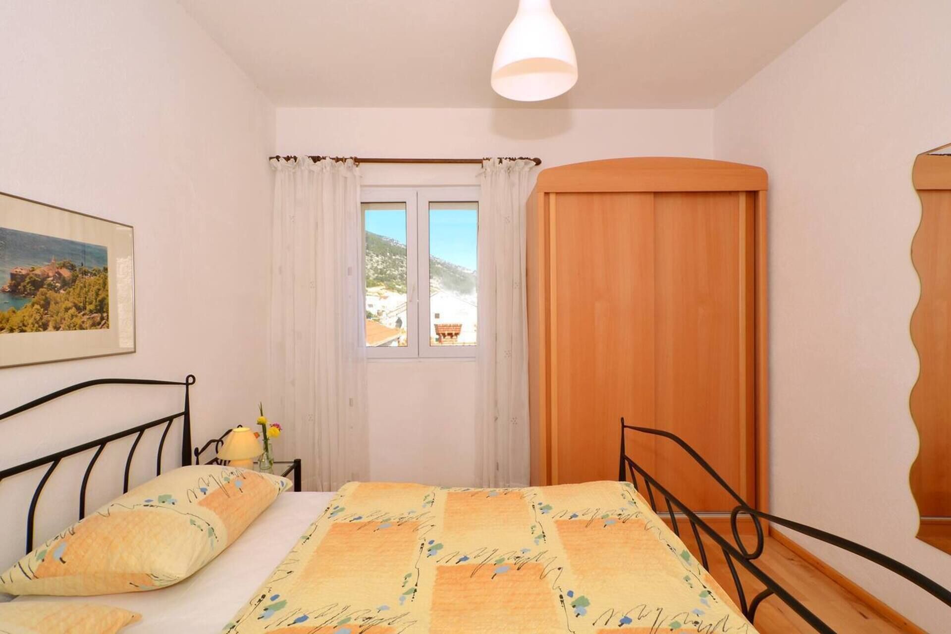 Ein Schlafzimmer mit Bett, einem Fenster mit Vorhängen, einer Holztür und einem Gemälde an der Wand.