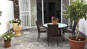 Eine Terrasse mit rundem Tisch und Stühlen, Blumentöpfen und einem überdachten Sitzbereich.