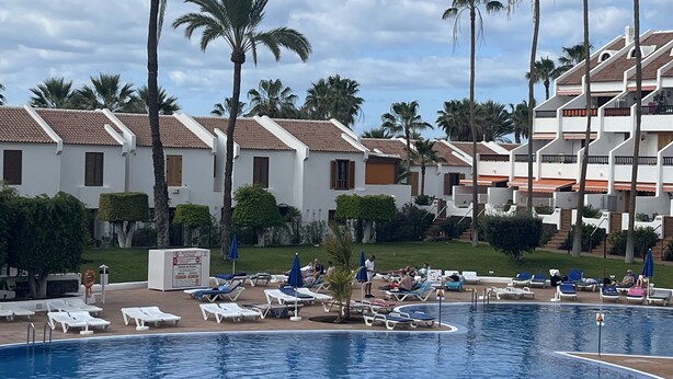 Ein Poolbereich mit Liegestühlen und einem Schwimmbecken, umgeben von Palmen und Hotelgebäuden.