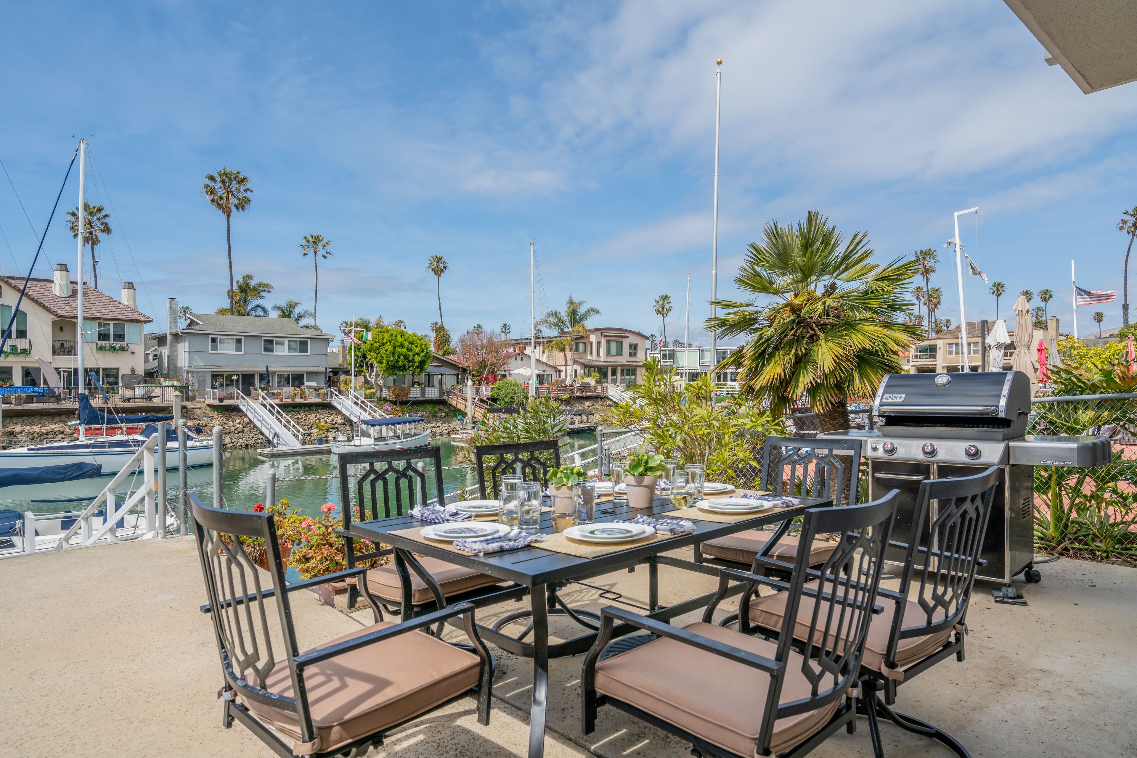 An outdoor dining area with a table set for four, overlooking a marina with boats and houses.
