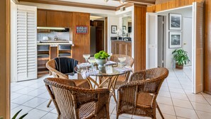 Un coin repas avec des chaises en osier et une table en verre, une cuisine avec des meubles en bois et une porte sur laquelle est apposée une pancarte.