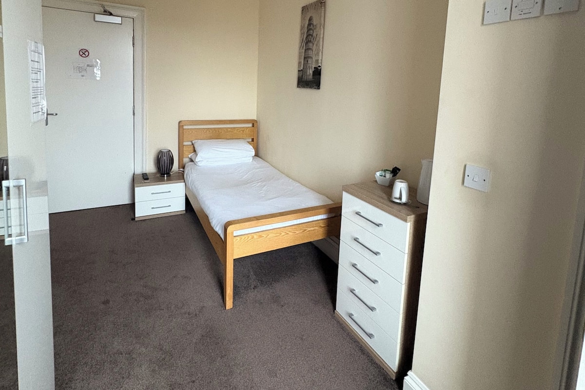Un dormitorio con una cama individual, mesitas de noche, una lámpara de pared y una puerta con picaporte.