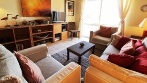 Una sala de estar con sofá, sillones, una mesa de centro, televisor y estantería.
