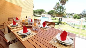 Mesa de comedor con platos, vasos y servilletas, con vista a una piscina y palmeras.