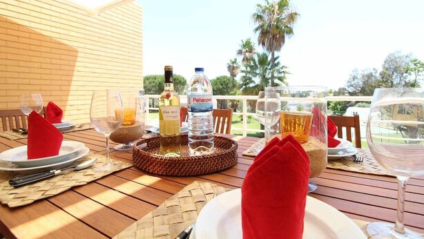 Un área de comedor al aire libre con una mesa preparada para dos personas, que incluye una bandeja de mimbre, platos, cubiertos y vasos.
