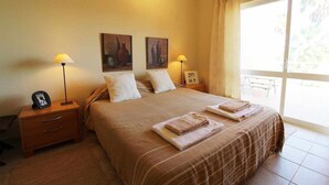 Una habitación de hotel con una cama, dos lámparas de noche, una mesita de noche con un teléfono y una ventana con cortinas.