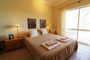 A hotel room with a bed, two bedside lamps, a nightstand with a phone, and a window with curtains.