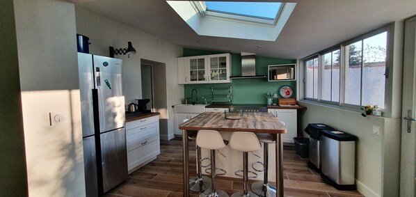 A compact kitchen with a skylight, white cabinets, a wooden island with bar stools, and a trash bin.
