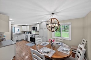 A modern kitchen with white cabinets, a dining area with a wooden table, and a chandelier.