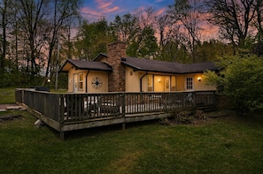 A two-story house with a deck, a brick chimney, and a large window.
