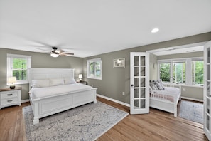 A bedroom with a large bed, a ceiling fan, and a view through an open door.