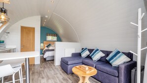 A modern loft-style room with a curved ceiling, a sofa with striped cushions, a wooden coffee table, and a white bar stool. - Dragonfly - sleeps 2 guests  in 1 bedroom (Norwich)